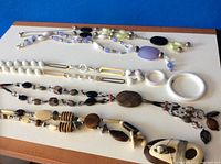 Top view of all seven vintage necklaces laid out flat on blue surface showing variety of bead styles and pendants.