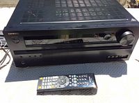 Black Onkyo TX-NR545 receiver viewed frontally alongside its black remote control placed in front.
