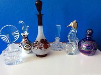 Front view of all six vintage perfume bottles lined up showing their different shapes, sizes and stoppers in front of a blue background.