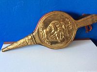 Side view of the vintage fireplace bellows showing embossed ship design on brass.