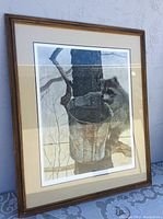 Framed picture showing raccoon holding a bucket against a tree with a wooden gold finish frame and beige mat.
