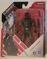 Front view of packaged Snake Eyes action figure with ninja outfit and weapons visible.