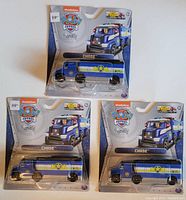 Three new Paw Patrol Chase trucks in original packaging, arranged in a group, showing brand and scale.