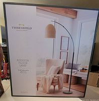 Photo of the Threshold Addison Floor Lamp packaging box showing the product image, brand, and features including the on/off rotary switch, black finish, and rattan shade.