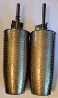 Two hand-hammered metallic toilet brush holders side by side