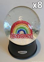 Front view of a musical water globe showing a rainbow with the phrase 'LOVE IS LOVE' inside a clear globe on a black base marked '2022'.