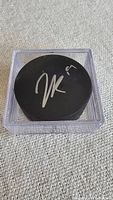 Top view of black hockey puck signed in silver marker, inside clear hard plastic case.