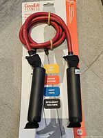 Front view of red resistance band coiled with black foam handles, mounted on GoodLife Fitness packaging showing resistance chart.