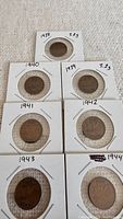 Close-up of Canadian pennies dated 1938, 1940, 1939, 1941, 1942, 1943, and 1944 in white cardboard holders.
