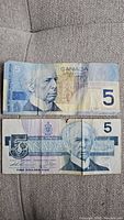 Front view of two Canadian 5 dollar bills, top 2002 series and bottom 1986 series, both heavily worn.