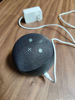 Charcoal fabric spherical Amazon Echo Dot 5th gen smart speaker on wood surface with power adapter and connected white power cable visible.