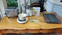 Photo of assorted kitchen items displayed on wooden desk including toaster, percolator, juicer, scales, drying rack, and can opener.