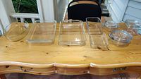 Photo of all glass bakeware and storage containers arranged on a wooden table showing their sizes and shapes clearly.