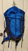Front view of blue Marmot Kompressor Verve 42 large backpack hanging on wall hook showing compact design with compression straps and front bungee system.