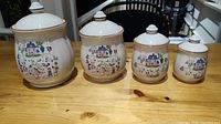 Four ceramic canisters of varying sizes arranged in a row on a wooden surface, each decorated with a farm-themed illustration.