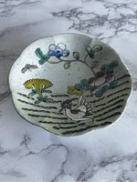Top view of antique Chinese footed porcelain bowl with hand painted Famille Rose floral and bird design with scalloped edge and crackled glaze.