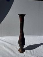 Full view of the slender brass vase showing its shape and detailed engraved patterns with red and gold accents.