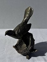 Front and side view of bronze bird perched on nest, showing detailed feather and nest texture with a heavy solid form.
