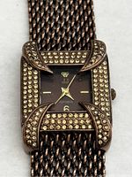 Front view showing the square brown watch face with rhinestone-set bezel and corner decorations, gold-tone crown logo, and hour markers.