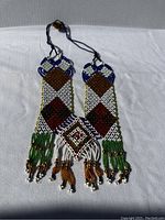 Photo of Awajún Enkepa breastplate necklace laid flat showing full design with detailed beadwork and tassels.