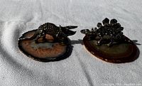 Two dinosaur figurines on agate stone bases shown together on a fabric surface.