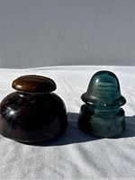 Two vintage pole insulators placed side by side on a white cloth background, one ceramic and one glass, photographed in natural light.