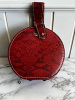 Front view of red circular textured bag with leather strap and white stitching on marble surface.