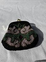 Front view of vintage square coin purse with detailed beadwork in black, green, white, gold, and red bead embellishment under sunlight.