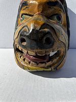 Front view of the vintage wooden animal mask showing the carved and painted face with an open mouth, teeth, eyes, and detailed coloration.