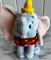 Front view of vintage stuffed Dumbo plush showing facial details, yellow hat and red collar with gold trim.