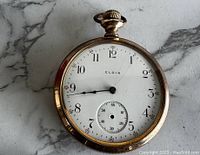 Front view of the vintage Elgin pocket watch showing white dial with Arabic numerals, black hands, and a subdial for seconds.