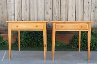 Full front view of two matching knotty pine end tables showing wood grain, drawer with brass pull, tapered legs.