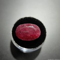 Close-up photo of the 15 carat red oval ruby gemstone on black velvet stand.