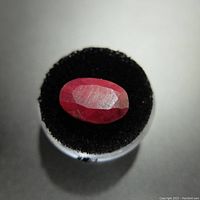 Top angle close-up of oval-shaped red ruby gemstone on black display stand, showing facets and color.