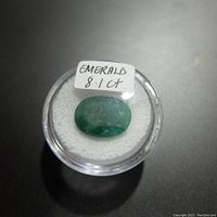 Top view of the 8.1 carat emerald gemstone in a clear round container with white padding and label.