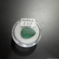 Top view of the pear-shaped emerald gemstone in a clear round container with a label indicating 8.3 carats.