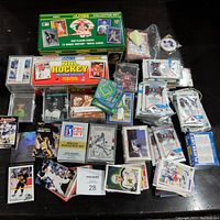 Wide shot of collection showing multiple boxes and loose stacks of vintage sports cards including hockey, baseball, football cards and unopened packs.