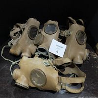 Four vintage rubber gas masks assembled together showing front view with eye lenses and filter attachments.