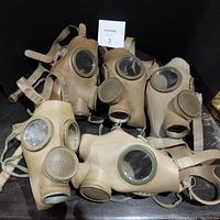 Five vintage gas masks displayed together showing overall exterior condition, eye lenses, and front filter area.