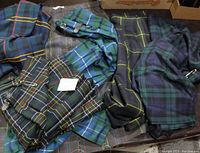 Several vintage Scottish tartan fabrics and kilts, various traditional tartan patterns and colors, laid out to show differences and accessories such as buckles and straps.