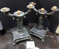 Pair of vintage metal candlestick holders showing overall design, square base, fluted column, two arms holding candle cups with cork stoppers.