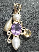 Silver pendant on black textured background showing amethyst, pearls, and yellow gemstone
