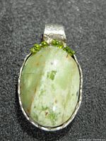 Close-up of oval green gemstone pendant accented with small peridot stones, silver bezel, and textured bail.
