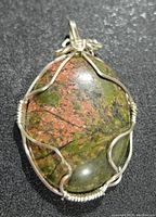 Close-up front view of the oval polished multicolor gemstone pendant wrapped with silver wire.