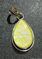Close-up image of the yellow iridescent pear-shaped gemstone set in silver with decorative bail detail.