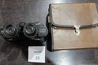 Vintage black textured binoculars with silver trim and markings 7x-12x 40 showing focus adjustment mechanism on wooden surface with MaxSold tag.