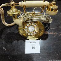 Front view showing rotary dial, brass base, and handset with coiled cord.