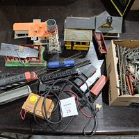 Overview of vintage train set components showing locomotives, train cars, tracks, control box, and model buildings including a water tower and station parts.