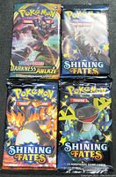 Front view of four sealed Pokémon booster packs: one Sword & Shield Darkness Ablaze and three Shining Fates.