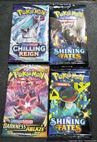 Front view of four sealed Pokémon TCG booster packs: Sword & Shield Chilling Reign, Sword & Shield Darkness Ablaze, and two Shining Fates.